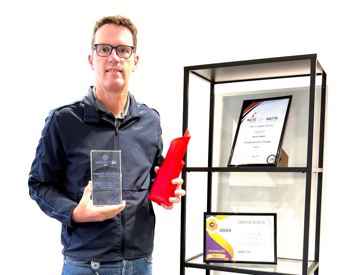 Kristen Britz holding an iAwards trophy beside a shelf of innovation awards